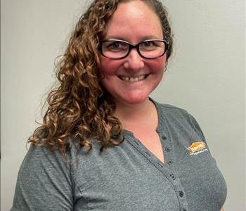 Brown-eyed, curly headed lady wearing black frame glasses and a blue blouse