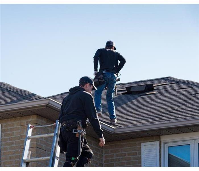 Two men on top of a roof doing inspection of the roof