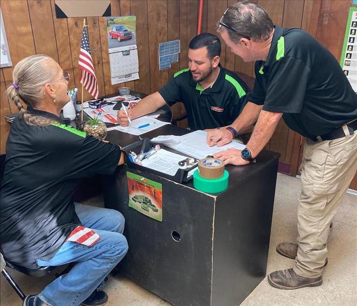 three servpro workers in heroready polo shirts sitting at a desk doing paperwork